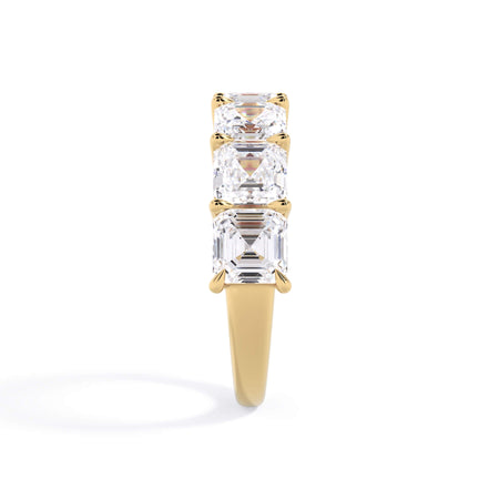 A picture of a seven stone diamond wedding ring with asscher cut diamonds that are shared prong set in yellow gold on a white background with a side profile view.