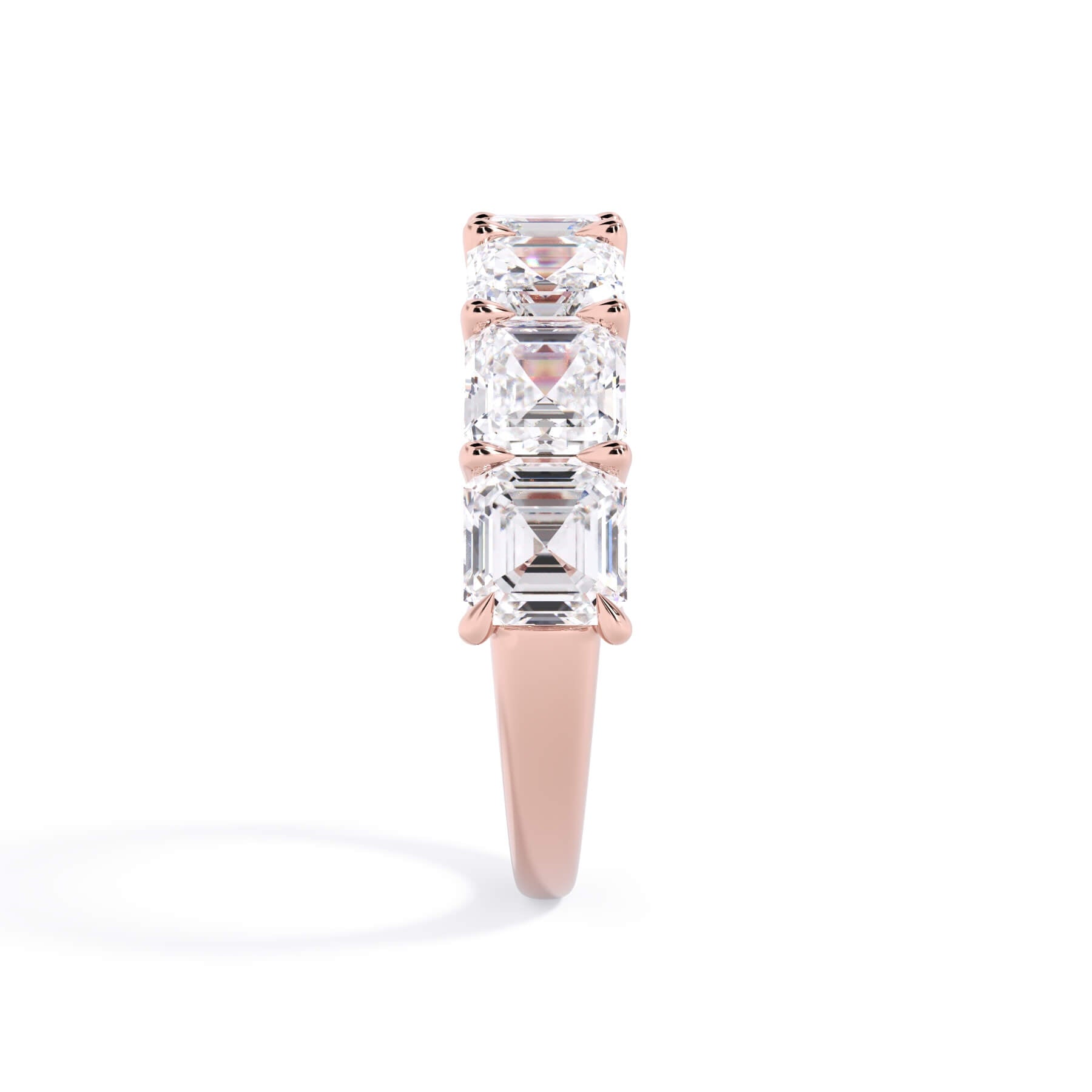 A picture of a seven stone diamond wedding ring with asscher cut diamonds that are U prong set in rose gold on a white background with a side profile view.