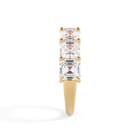A picture of a seven stone diamond wedding ring with asscher cut diamonds that are U prong set in yellow gold on a white background with a side profile view.