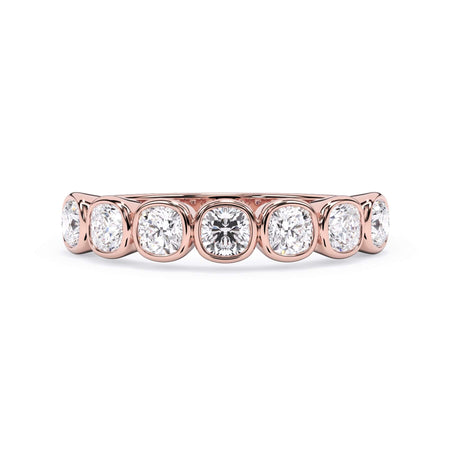 A picture of a seven stone diamond wedding ring with cushion cut diamonds that are bezel set in rose gold on a white background with the ring facing forward, lying down.