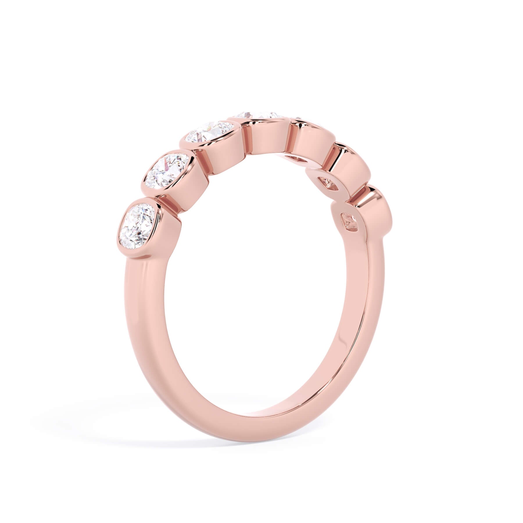 A picture of a seven stone diamond wedding ring with cushion cut diamonds that are bezel set in rose gold on a white background with a slightly angled, through the finger view.
