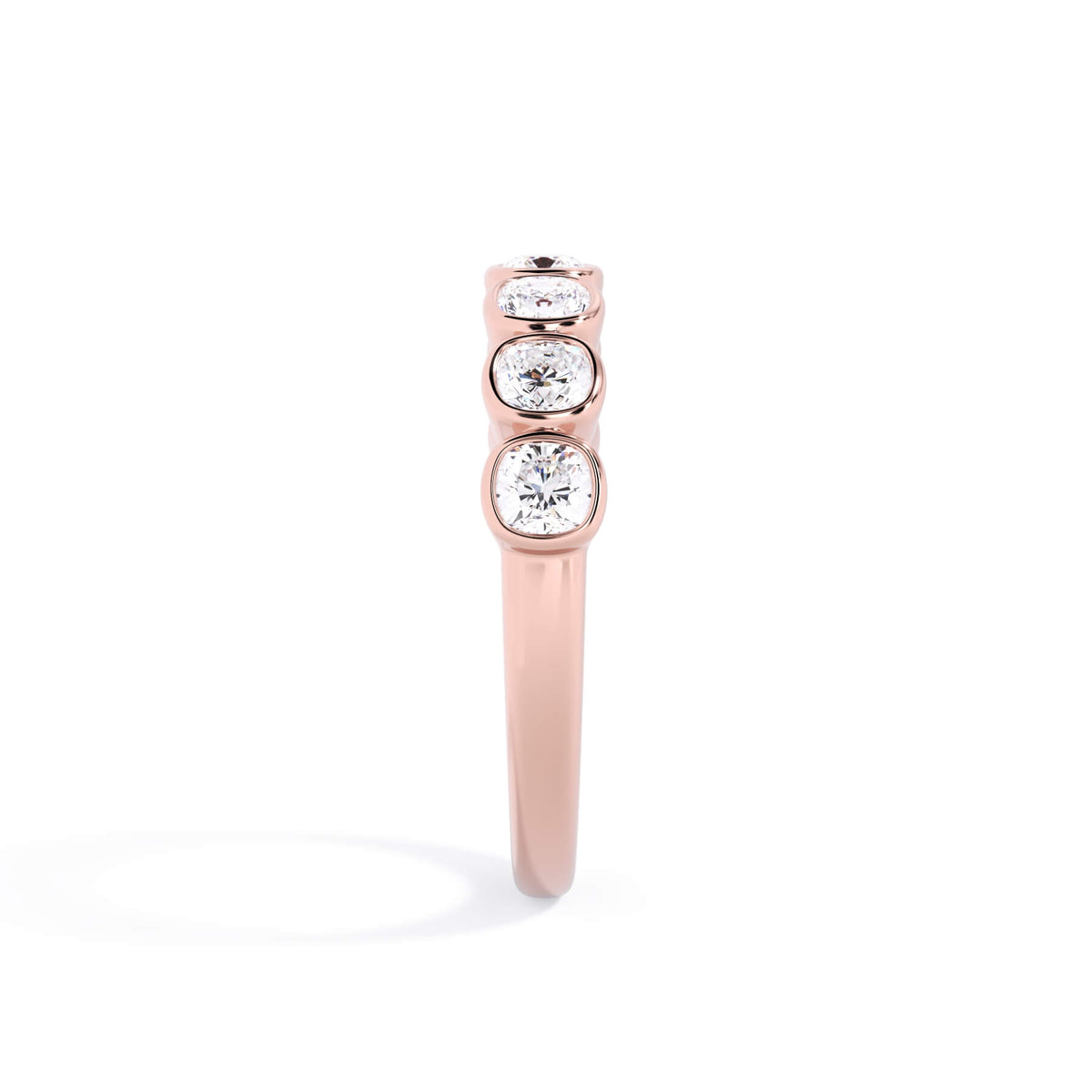 A picture of a seven stone diamond wedding ring with cushion cut diamonds that are bezel set in rose gold on a white background with a side profile view.