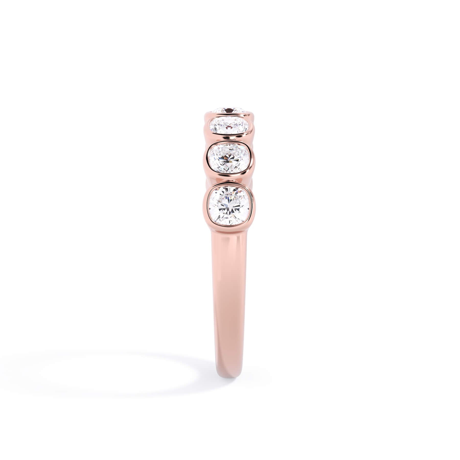 A picture of a seven stone diamond wedding ring with cushion cut diamonds that are bezel set in rose gold on a white background with a side profile view.