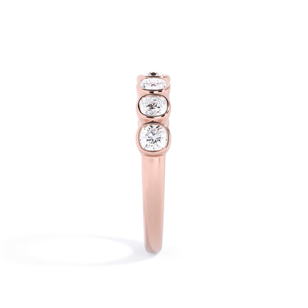 A picture of a seven stone diamond wedding ring with cushion cut diamonds that are bezel set in rose gold on a white background with a side profile view.