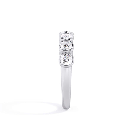 A picture of a seven stone diamond wedding ring with cushion cut diamonds that are bezel set in white gold or platinum on a white background with a side profile view.