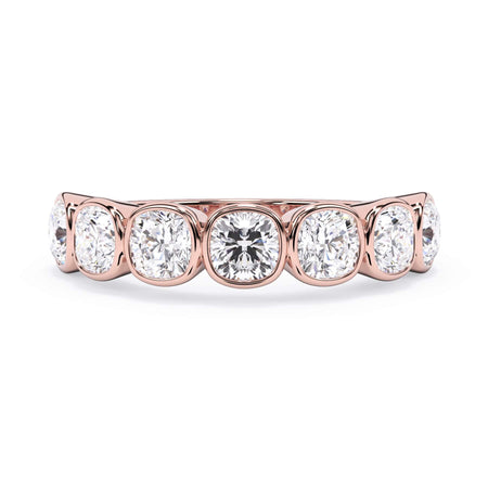 A picture of a seven stone diamond wedding ring with cushion cut diamonds that are bezel set in rose gold on a white background with the ring facing forward, lying down.