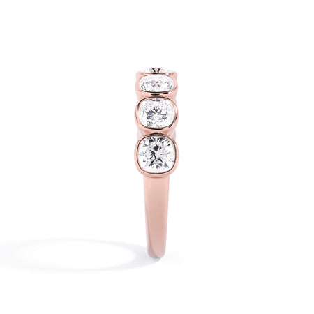 A picture of a seven stone diamond wedding ring with cushion cut diamonds that are bezel set in rose gold on a white background with the ring facing forward, lying down.