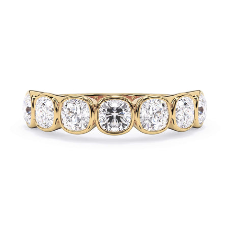 A picture of a seven stone diamond wedding ring with cushion cut diamonds that are bezel set in yellow gold on a white background with the ring facing forward, lying down.