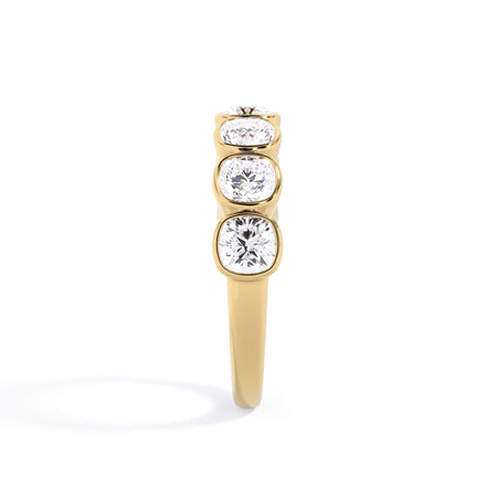 A picture of a seven stone diamond wedding ring with cushion cut diamonds that are bezel set in yellow gold on a white background with a side profile view.