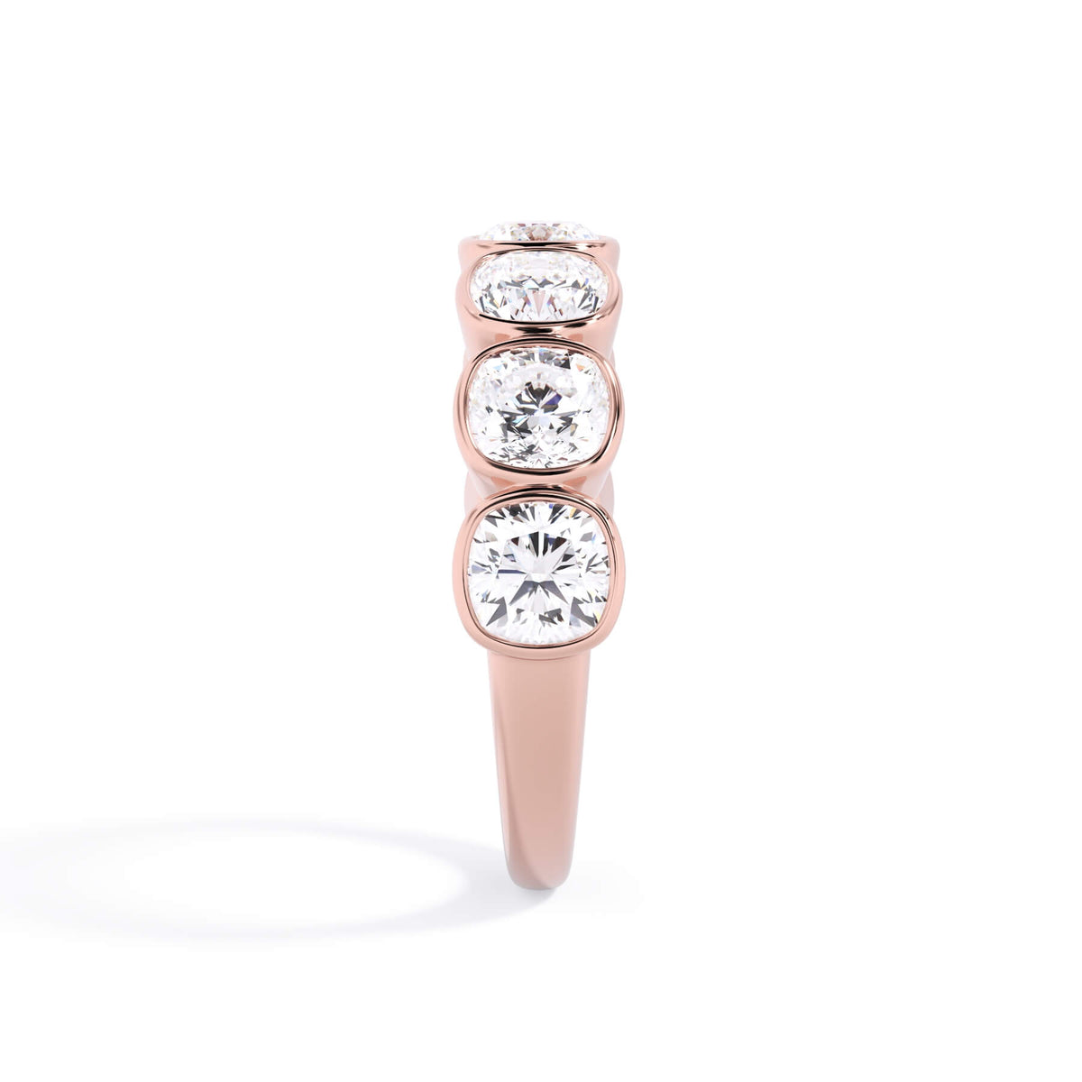 A picture of a seven stone diamond wedding ring with cushion cut diamonds that are bezel set in rose gold on a white background with a side profile view.