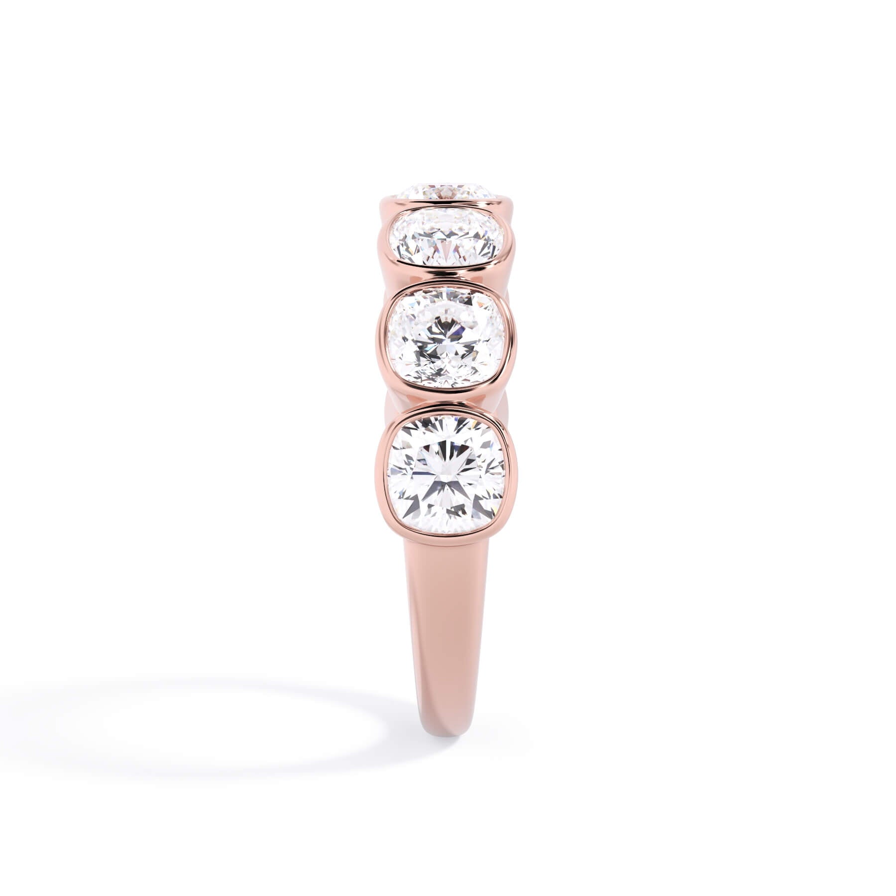 A picture of a seven stone diamond wedding ring with cushion cut diamonds that are bezel set in rose gold on a white background with a side profile view.