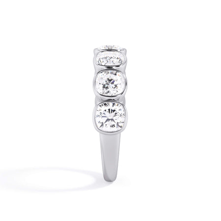 A picture of a seven stone diamond wedding ring with cushion cut diamonds that are bezel set in white gold or platinum on a white background with a side profile view.