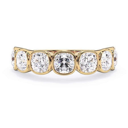 A picture of a seven stone diamond wedding ring with cushion cut diamonds that are bezel set in yellow gold on a white background with the ring facing forward, lying down.