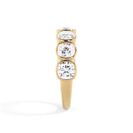 A picture of a seven stone diamond wedding ring with cushion cut diamonds that are bezel set in yellow gold on a white background with a side profile view.