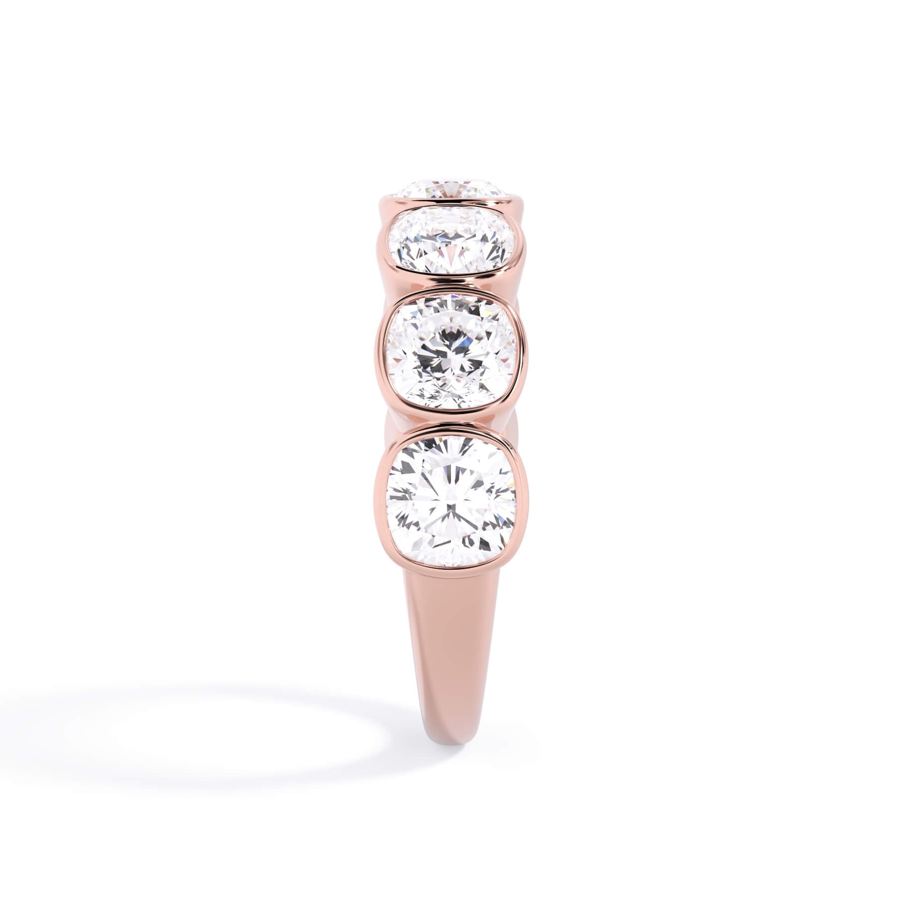A picture of a seven stone diamond wedding ring with cushion cut diamonds that are bezel set in rose gold on a white background with a side profile view.
