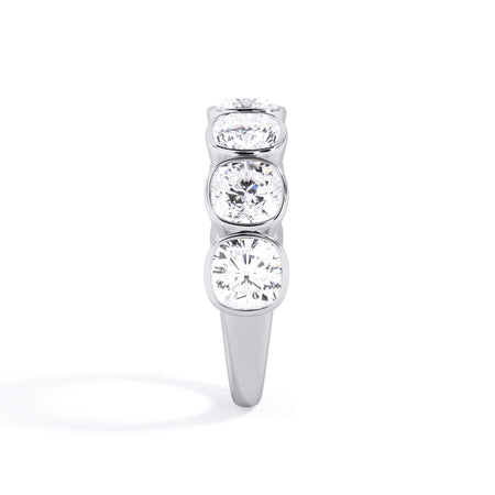 A picture of a seven stone diamond wedding ring with cushion cut diamonds that are bezel set in white gold or platinum on a white background with a side profile view.