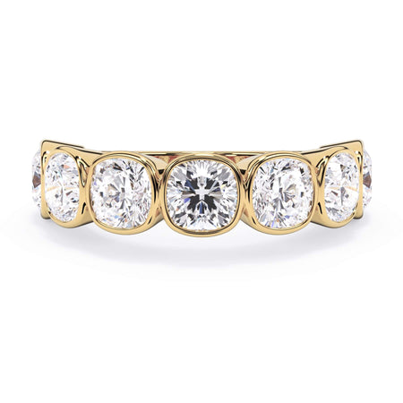 A picture of a seven stone diamond wedding ring with cushion cut diamonds that are bezel set in yellow gold on a white background with the ring facing forward, lying down.