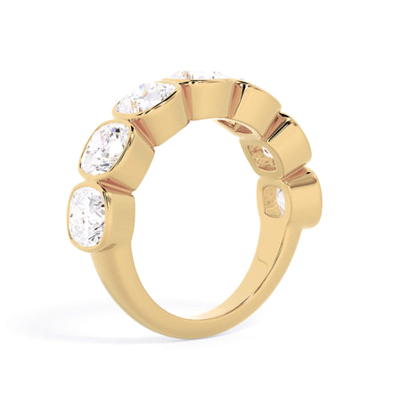 A picture of a seven stone diamond wedding ring with cushion cut diamonds that are bezel set in yellow gold on a white background with a slightly angled, through the finger view.