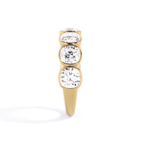 A picture of a seven stone diamond wedding ring with cushion cut diamonds that are bezel set in yellow gold on a white background with a side profile view.