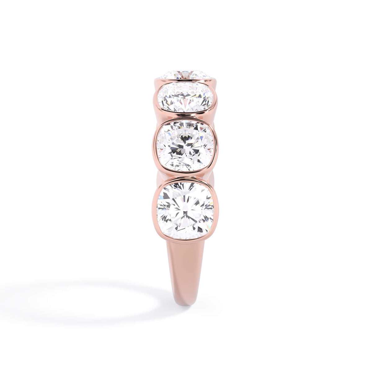 A picture of a seven stone diamond wedding ring with cushion cut diamonds that are bezel set in rose gold on a white background with a side profile view.