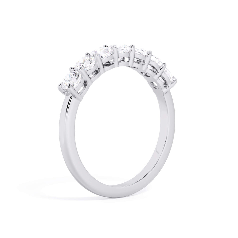 A picture of a seven stone diamond wedding ring with cushion cut diamonds that are shared prong set in white gold or platinum on a white background with a slightly angled, through the finger view.