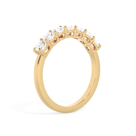A picture of a seven stone diamond wedding ring with cushion cut diamonds that are shared prong set in yellow gold on a white background with a slightly angled, through the finger view.