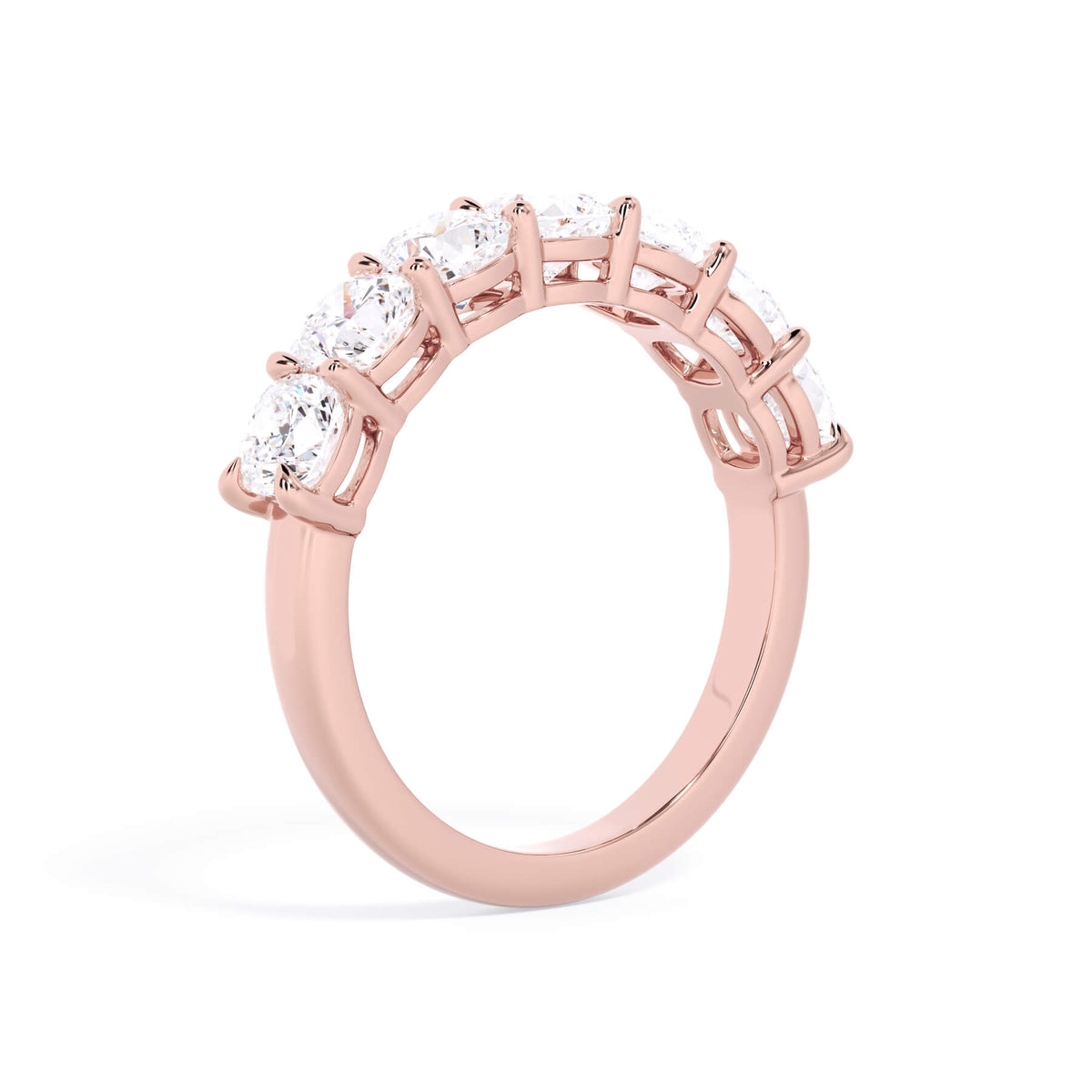 A picture of a seven stone diamond wedding ring with cushion cut diamonds that are shared prong set in rose gold on a white background with a slightly angled, through the finger view.