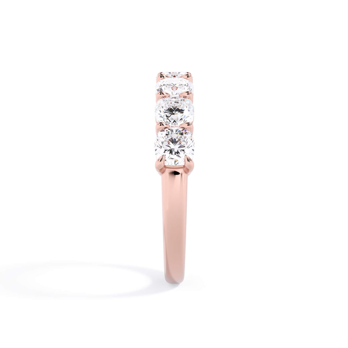 A picture of a seven stone diamond wedding ring with cushion cut diamonds that are shared prong set in rose gold on a white background with a side profile view.