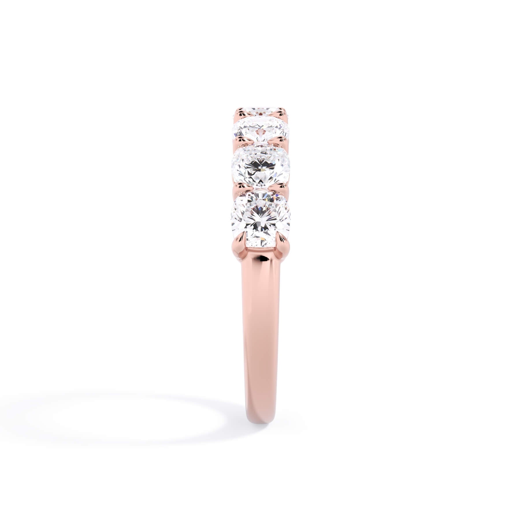 A picture of a seven stone diamond wedding ring with cushion cut diamonds that are shared prong set in rose gold on a white background with a side profile view.
