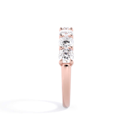 A picture of a seven stone diamond wedding ring with cushion cut diamonds that are shared prong set in rose gold on a white background with a side profile view.