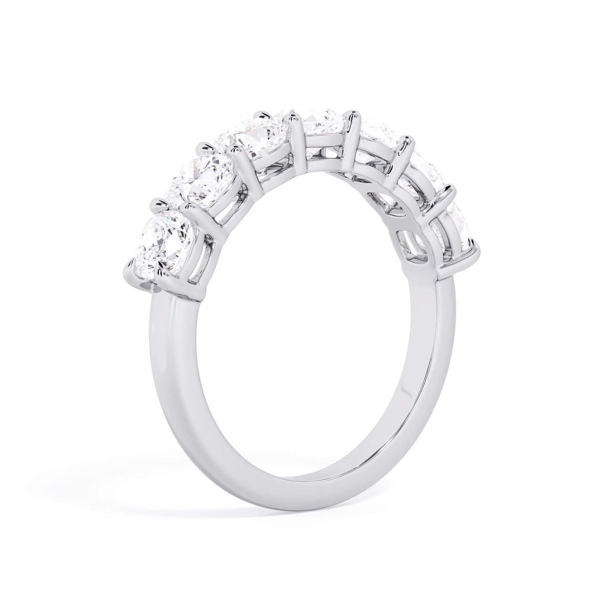 A picture of a seven stone diamond wedding ring with cushion cut diamonds that are shared prong set in white gold or platinum on a white background with a slightly angled, through the finger view.