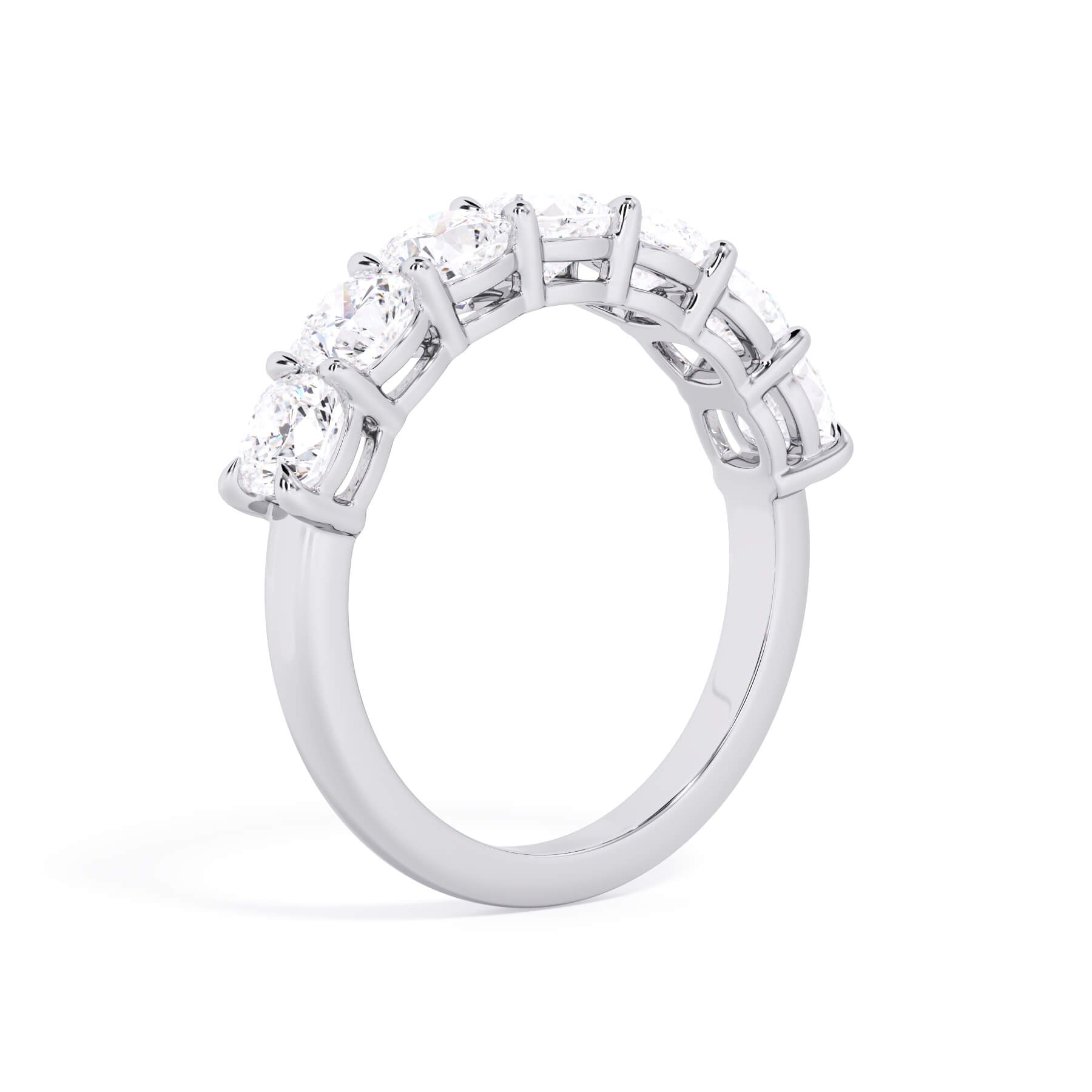 A picture of a seven stone diamond wedding ring with cushion cut diamonds that are shared prong set in white gold or platinum on a white background with a slightly angled, through the finger view.