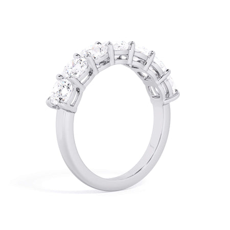 A picture of a seven stone diamond wedding ring with cushion cut diamonds that are shared prong set in white gold or platinum on a white background with a slightly angled, through the finger view.
