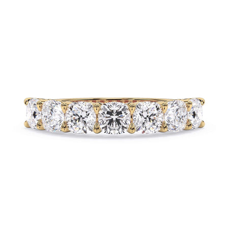 A picture of a seven stone diamond wedding ring with cushion cut diamonds that are shared prong set in yellow gold on a white background with the ring facing forward, lying down.