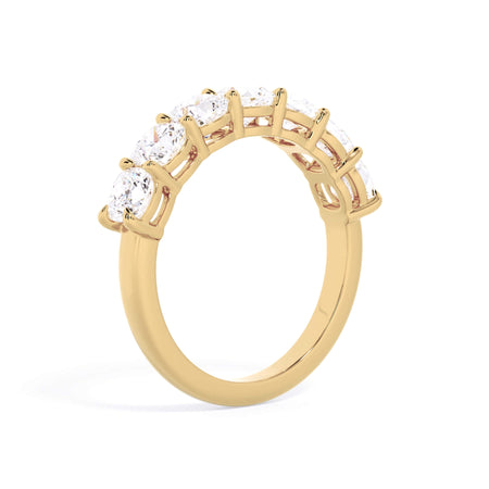 A picture of a seven stone diamond wedding ring with cushion cut diamonds that are shared prong set in yellow gold on a white background with a slightly angled, through the finger view.