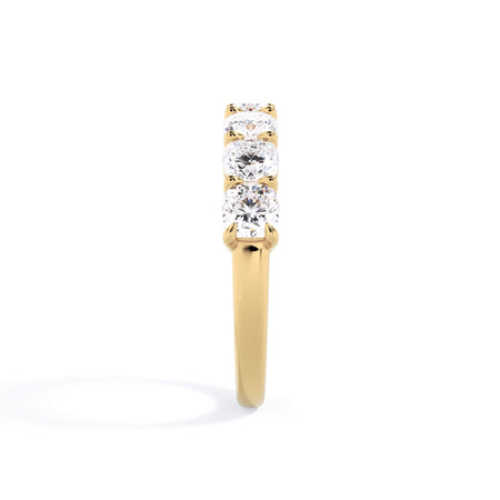 A picture of a seven stone diamond wedding ring with cushion cut diamonds that are shared prong set in yellow gold on a white background with a side profile view.