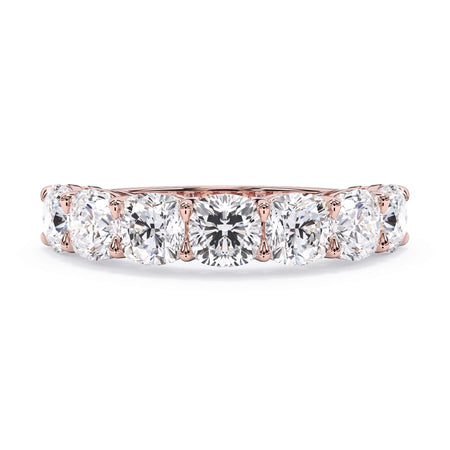 A picture of a seven stone diamond wedding ring with cushion cut diamonds that are shared prong set in rose gold on a white background with the ring facing forward, lying down.