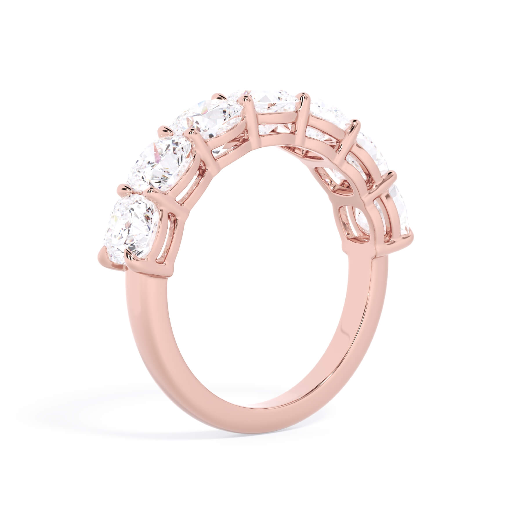 A picture of a seven stone diamond wedding ring with cushion cut diamonds that are shared prong set in rose gold on a white background with a slightly angled, through the finger view.