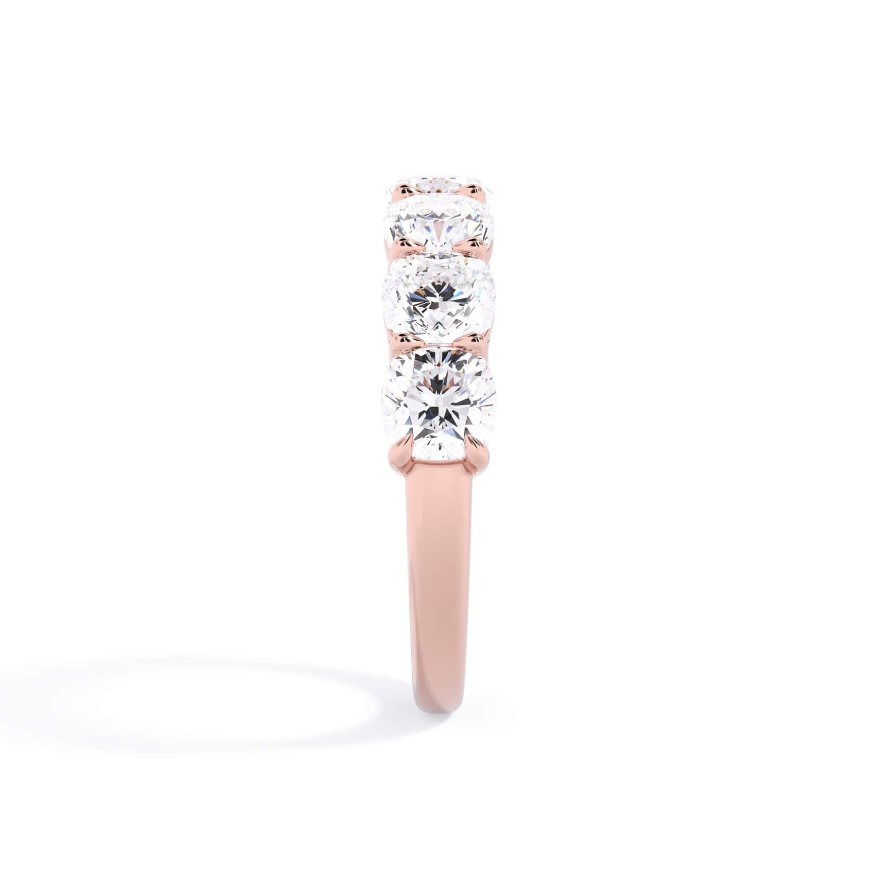 A picture of a seven stone diamond wedding ring with cushion cut diamonds that are shared prong set in rose gold on a white background with a side profile view.
