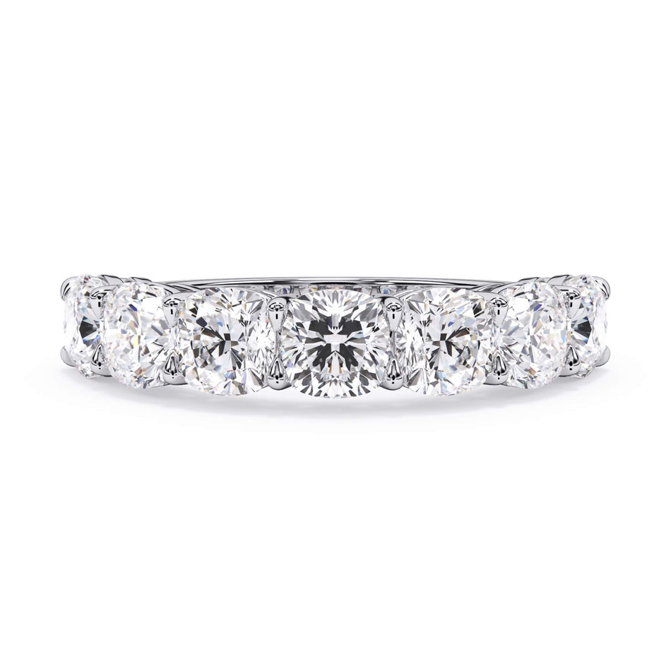 A picture of a seven stone diamond wedding ring with cushion cut diamonds that are shared prong set in white gold or platinum on a white background with the ring facing forward, lying down.