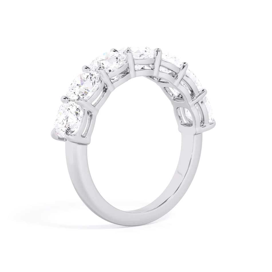A picture of a seven stone diamond wedding ring with cushion cut diamonds that are shared prong set in white gold or platinum on a white background with a slightly angled, through the finger view.