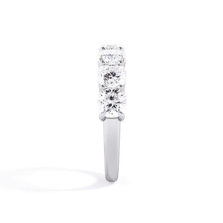 A picture of a seven stone diamond wedding ring with cushion cut diamonds that are shared prong set in white gold or platinum on a white background with a side profile view.