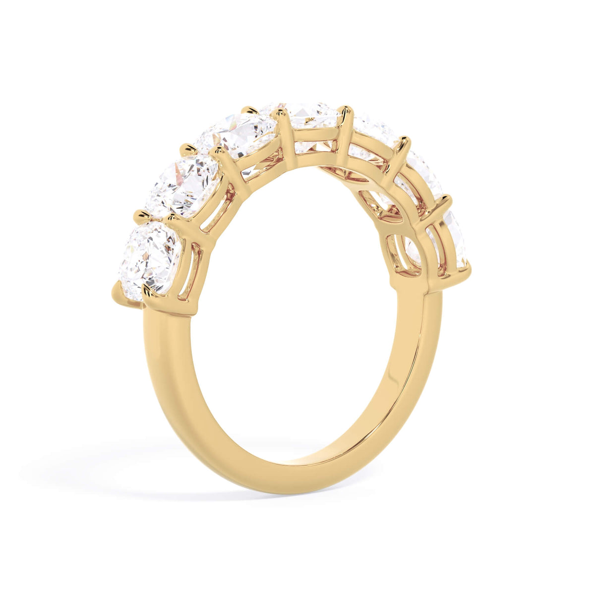 A picture of a seven stone diamond wedding ring with cushion cut diamonds that are shared prong set in yellow gold on a white background with a slightly angled, through the finger view.