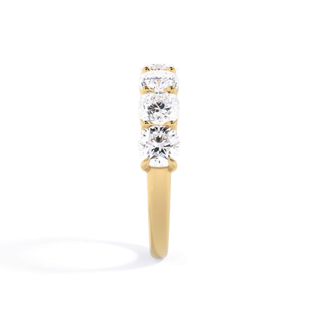 A picture of a seven stone diamond wedding ring with cushion cut diamonds that are shared prong set in yellow gold on a white background with a side profile view.