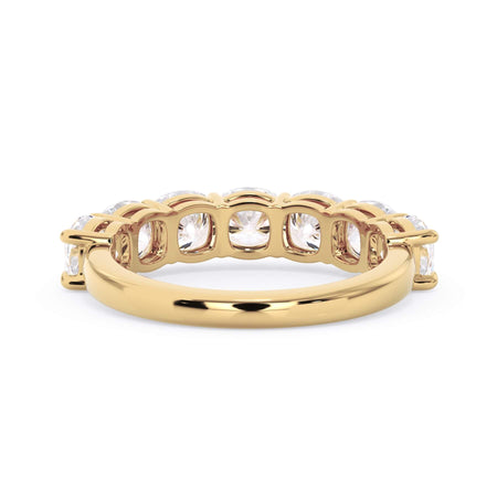 A picture of a seven stone diamond wedding ring with cushion cut diamonds that are shared prong set in yellow gold on a white background with a view of the underside of the ring.