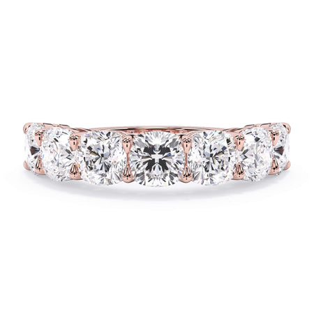 A picture of a seven stone diamond wedding ring with cushion cut diamonds that are shared prong set in rose gold on a white background with the ring facing forward, lying down.