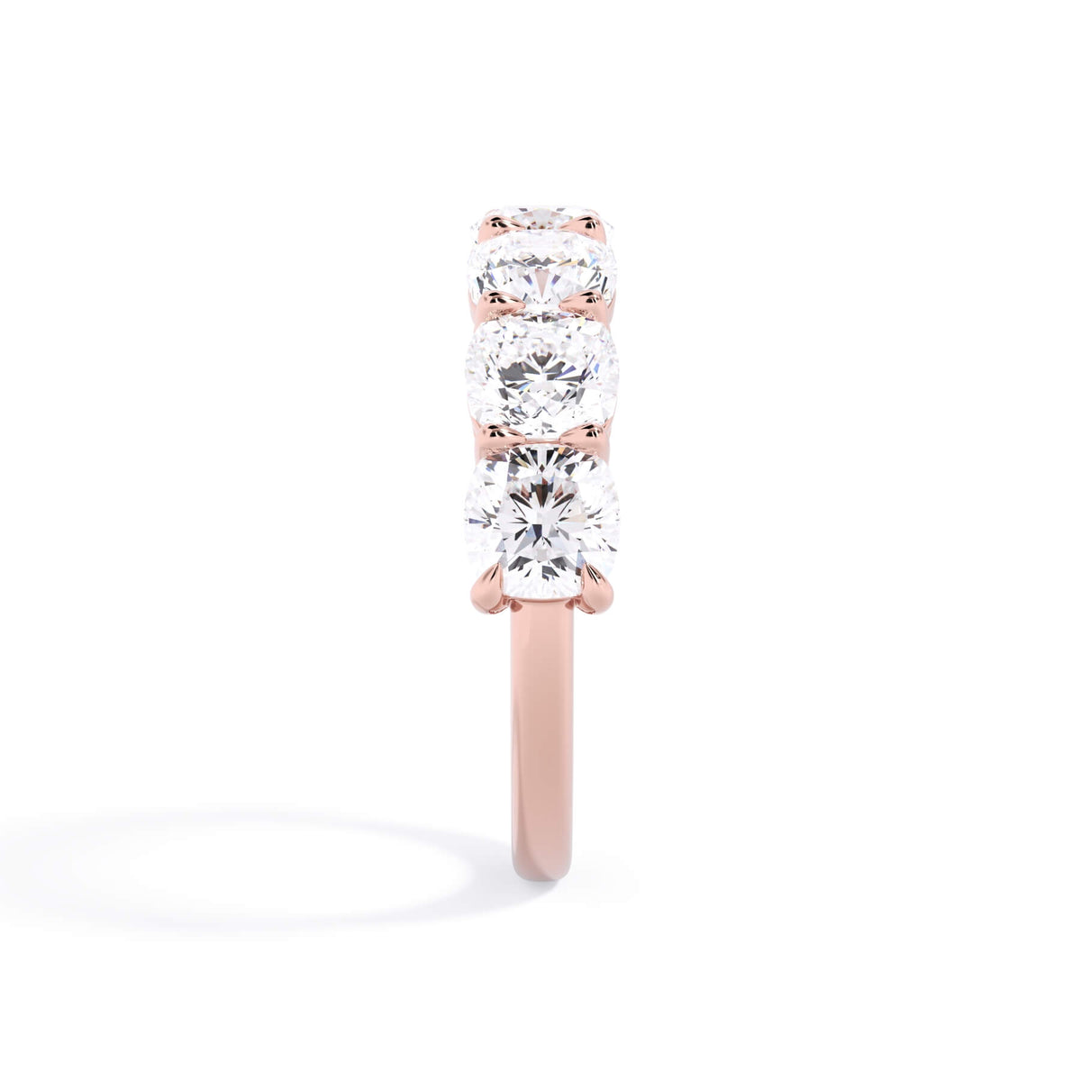 A picture of a seven stone diamond wedding ring with cushion cut diamonds that are shared prong set in rose gold on a white background with a side profile view.