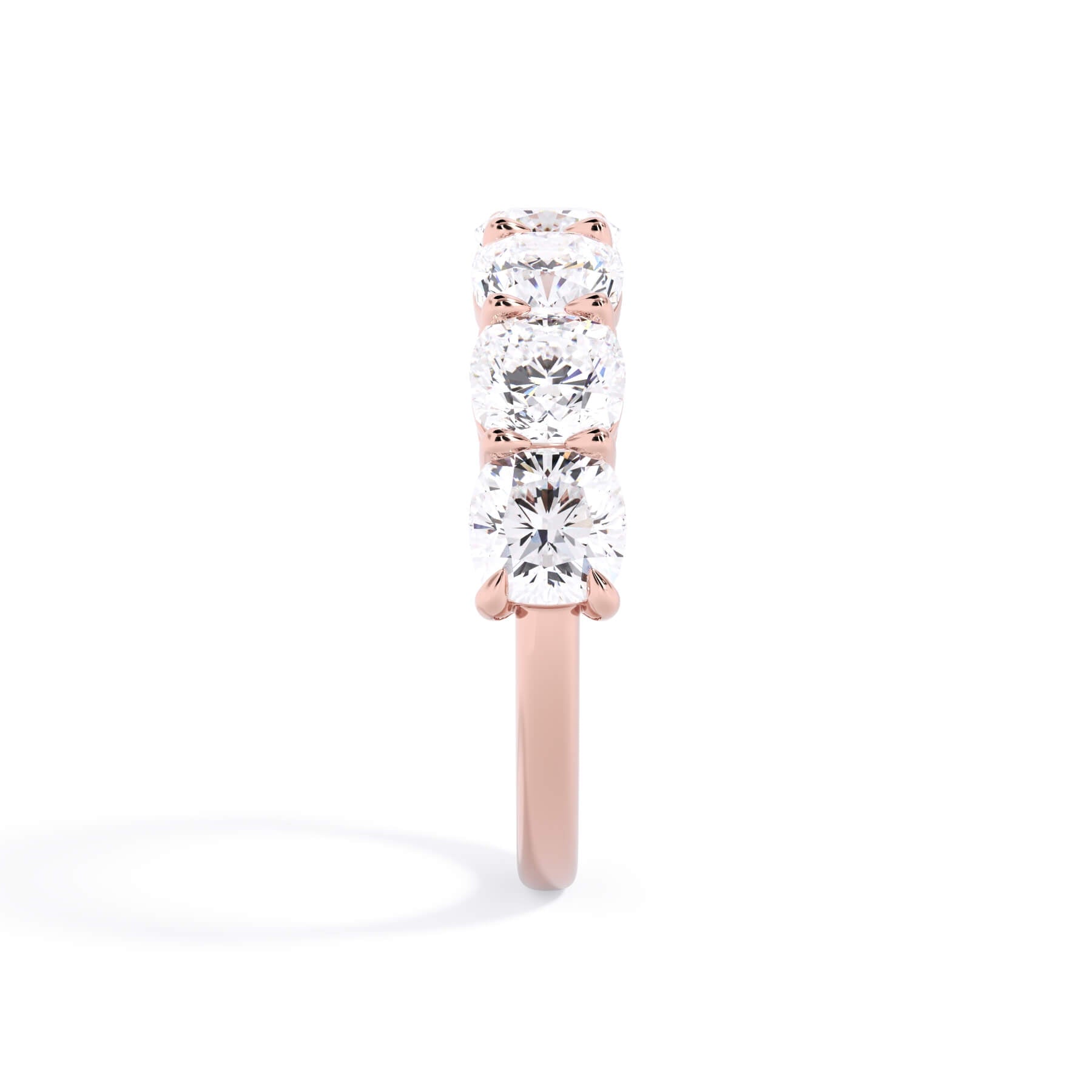 A picture of a seven stone diamond wedding ring with cushion cut diamonds that are shared prong set in rose gold on a white background with a side profile view.