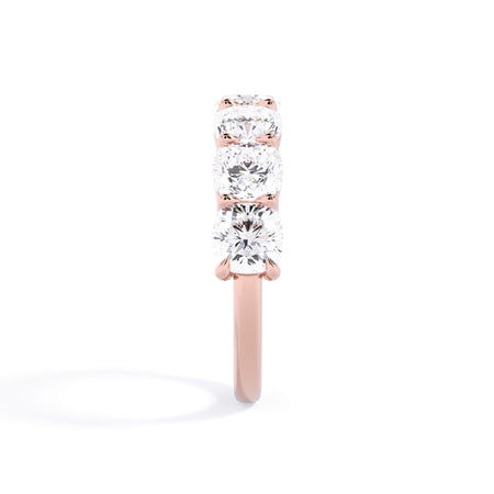 A picture of a seven stone diamond wedding ring with cushion cut diamonds that are shared prong set in rose gold on a white background with a side profile view.