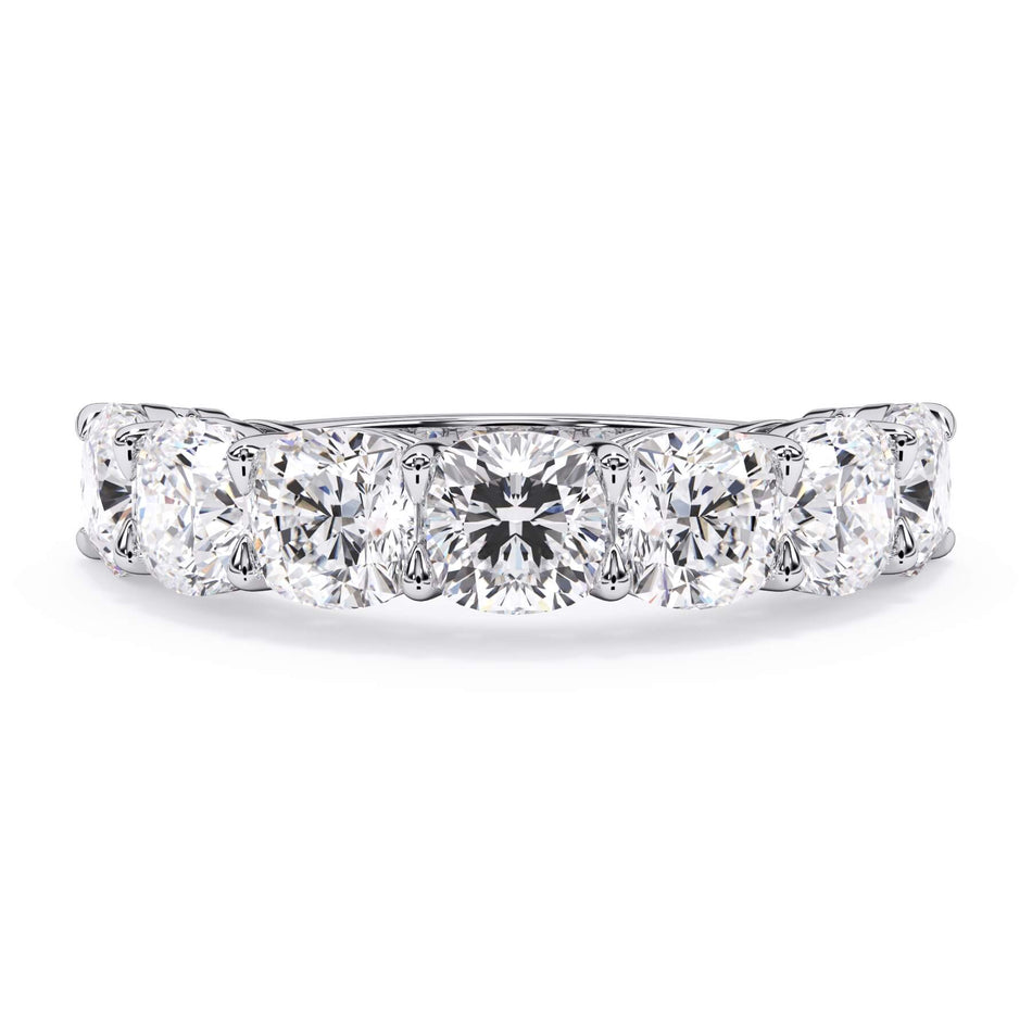 A picture of a seven stone diamond wedding ring with cushion cut diamonds that are shared prong set in white gold or platinum on a white background with the ring facing forward, lying down.
